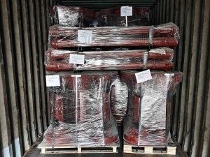 Stacked red cast iron lamp posts on wooden pallets inside shipping container