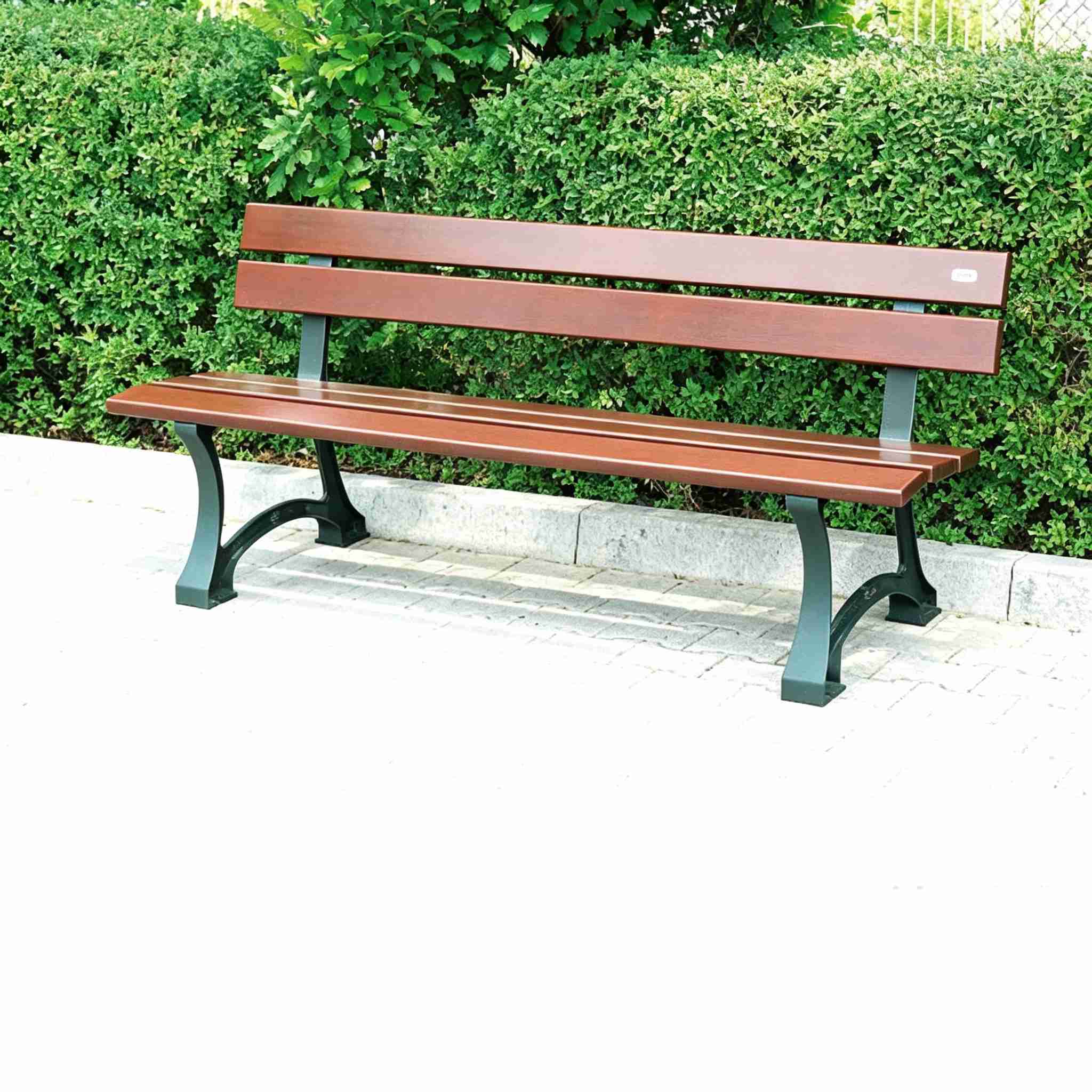 Brown wooden slat park bench with green ductile iron legs placed in garden beside green hedge